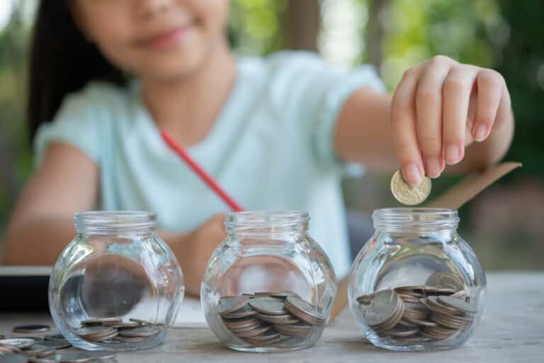 cute asian little girl playing with coins making stacks money kid saving money into piggy bank into glass jar child counting his saved coins children learning about future concept